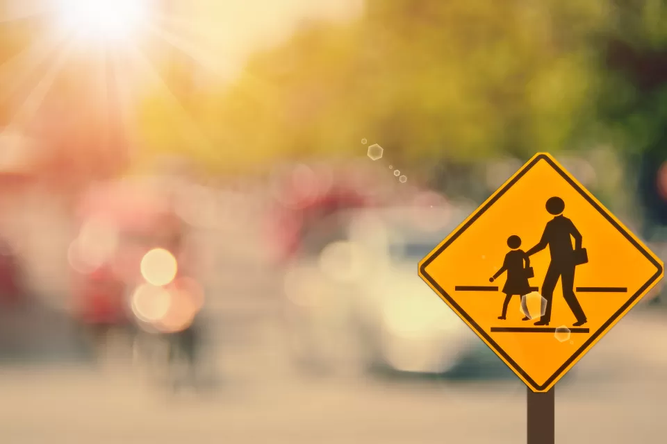 Yellow school corssing sign with two human figures against blurry background